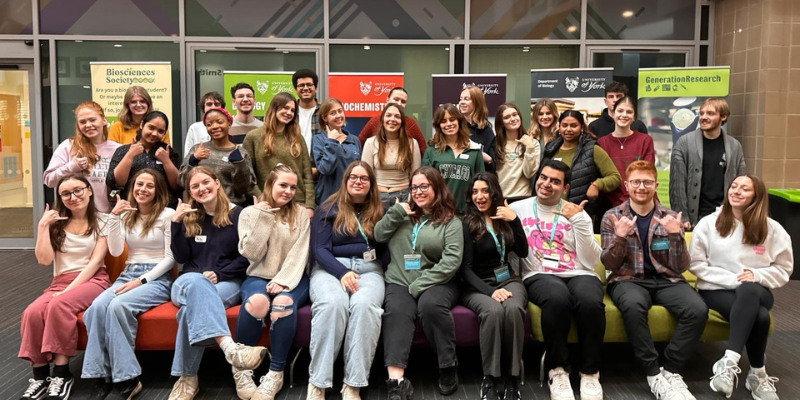 A group of students are smiling and posing with their hands shaped like phones